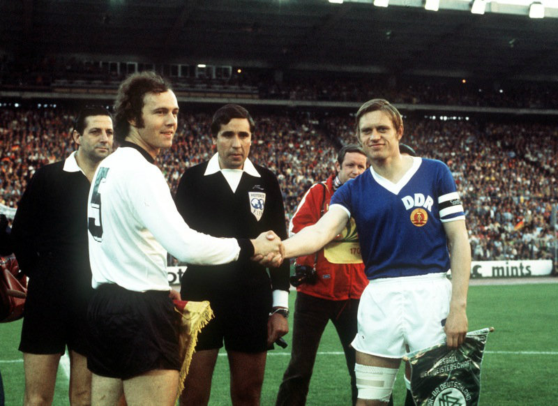 West Germany captain Franz Beckenbauer (l) shakes hands with East Germany captain Bernd Brausch (r) before the match, watched by referee Ramon Barreto Ruiz (c)